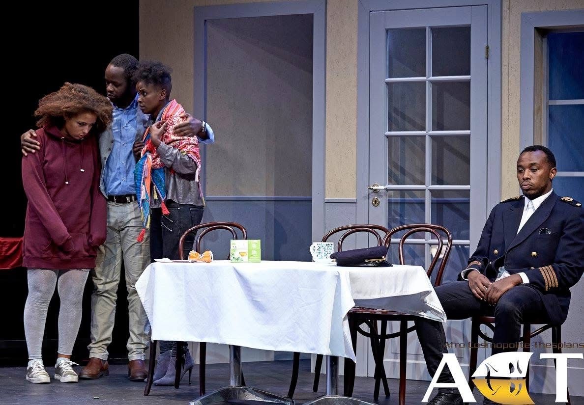 An Enemy of the People production image with a uniformed civic figure seated apart from a family group on stage.