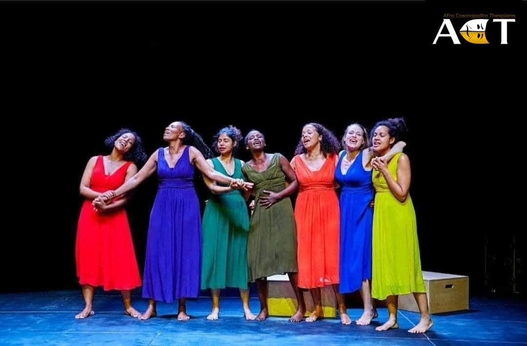 The ensemble standing together in vivid color dresses.
