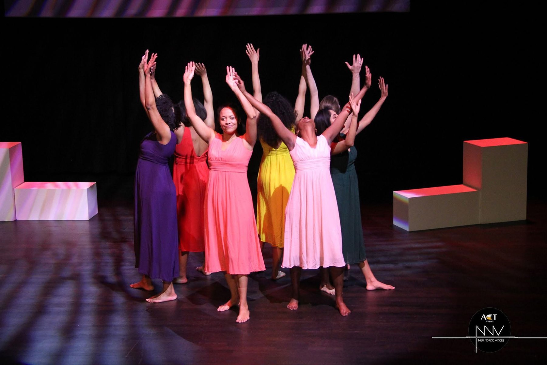 The ensemble of For Colored Girls forming a ritual circle with raised arms on stage.