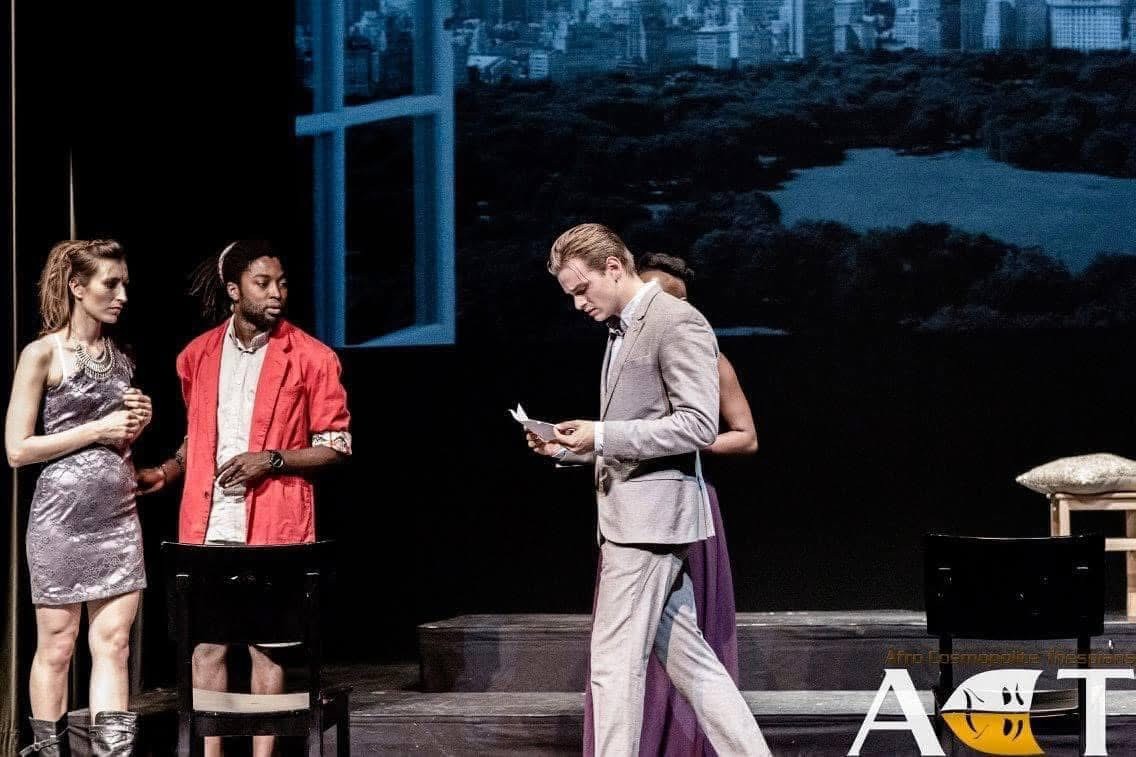 En figur læser fra et papir på scenen i The Merchant of Venice, mens andre ser til.