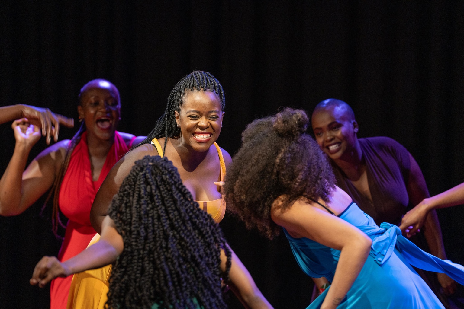 Close dance image of the ensemble in vivid dresses.