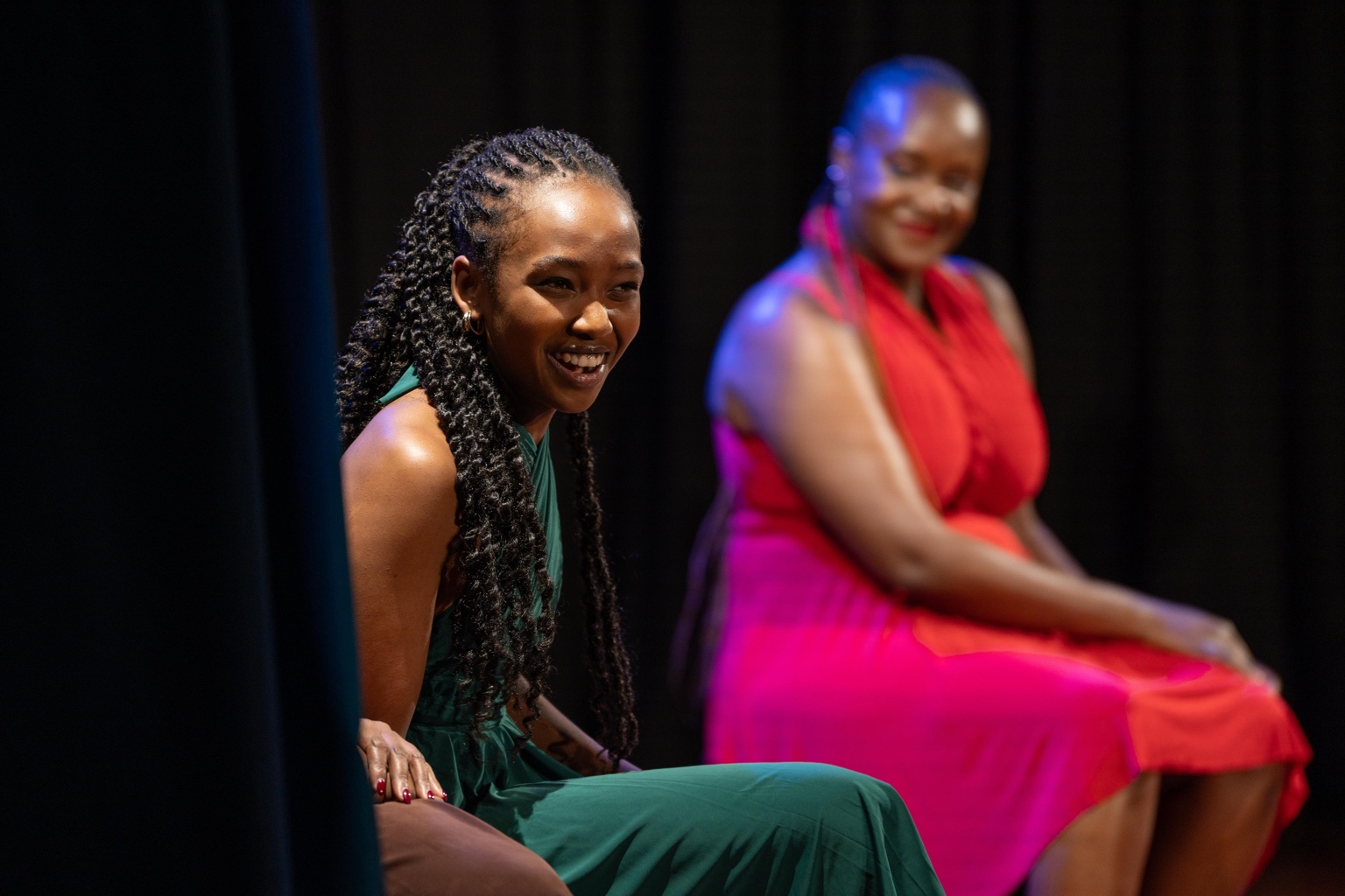 A woman in green smiling from the side of the stage.
