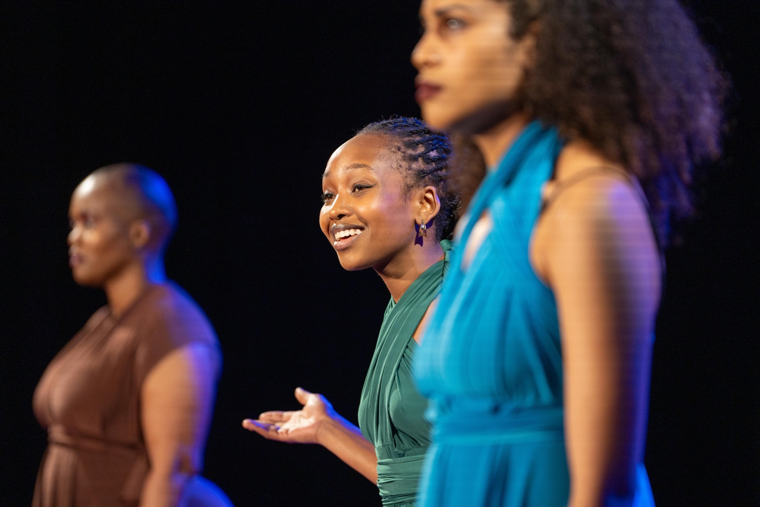 A woman in green speaking with another woman blurred in the foreground.